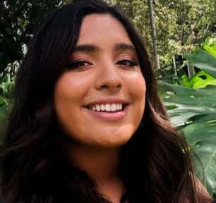 Pictured a young woman with long dark brown hair smiling at the camera. It's a headshhot and the background appears to be in a wooded area. Rodeo Swim VIP Coordinator, Stephanie Monroy